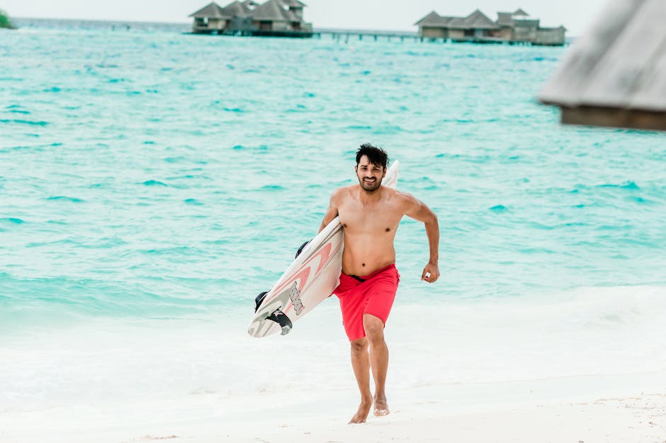 A man in red shorts joyfully runs on a Maldives beach carrying a surfboard